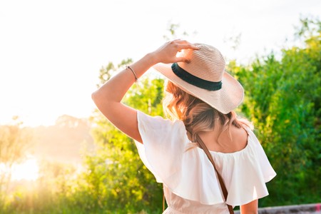 Woman holding her hat walking into the sun